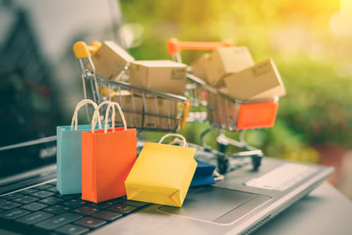 Miniature shopping carts full of boxes and colored shopping bags on a laptop keyboard.